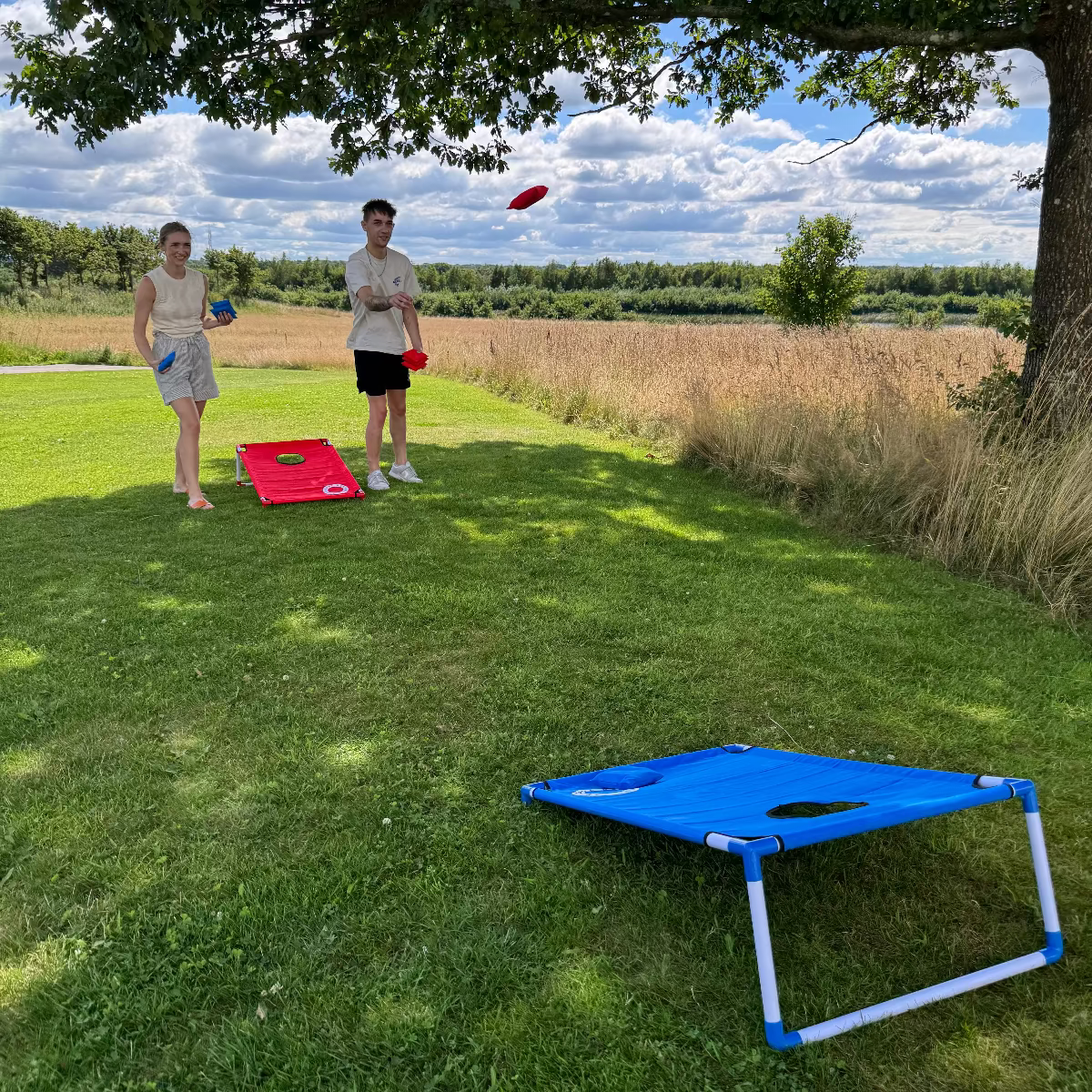 2 personer som spiller cornhole fra cornhole.dk med beach set strandsÊttet i pvc og stof, med rÞde og blÄ Êrteposer og cornholeposer