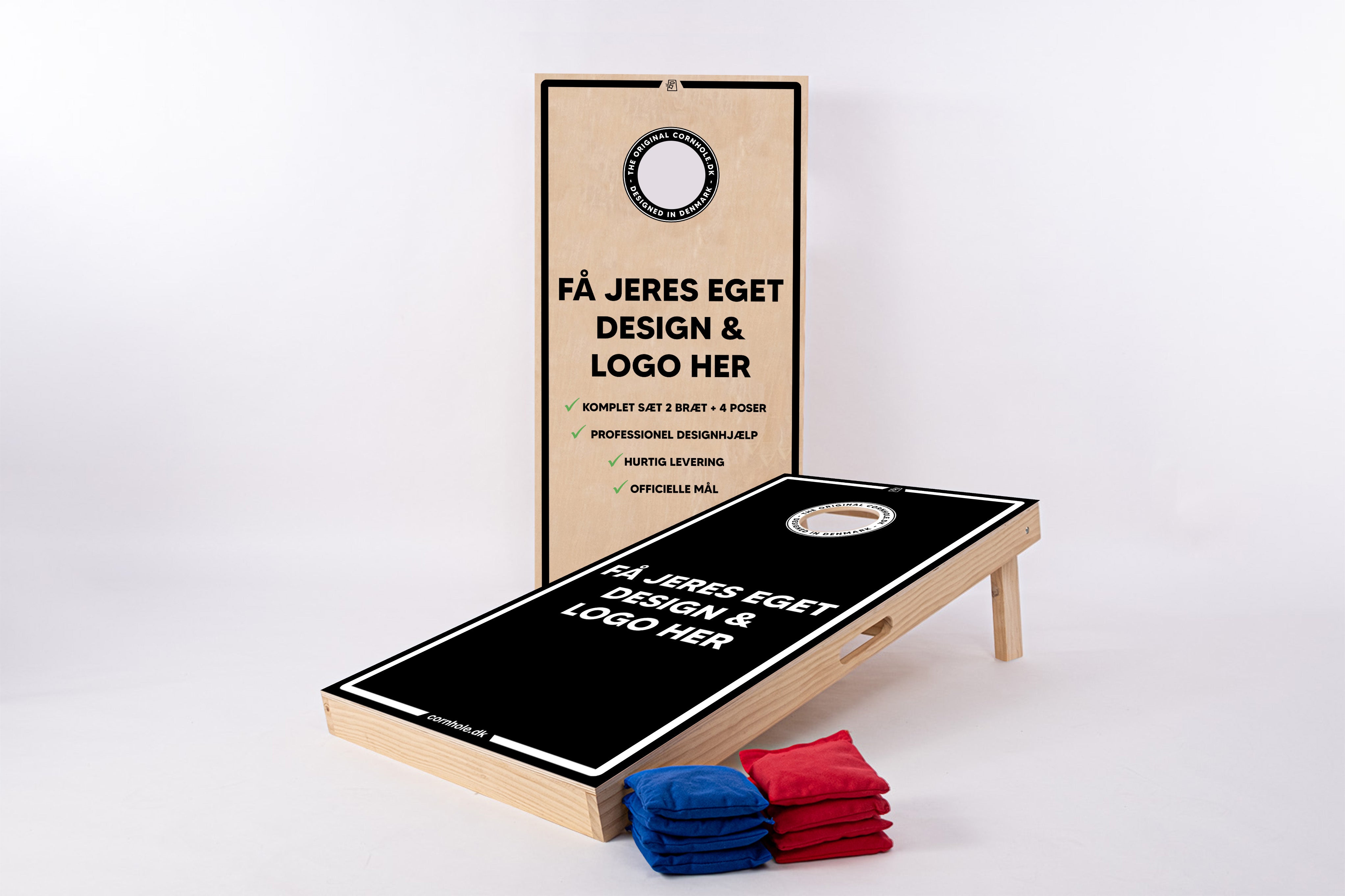 Et billede af et personligt tilpasset cornhole-spil med to brÊdder og otte bÞnnesÊkke i blÄ og rÞd. Det ene brÊt stÄr opret og viser en reklame for at fÄ sit eget design og logo med tekst pÄ dansk, mens det andet brÊt ligger fladt klar til spil. Det flade brÊt har et simpelt, stilfuldt sort design med en hvid kant og et hvidt mÄlomrÄde. BrÊdderne ser ud til at vÊre fremstillet af lyst trÊ med en naturlig finish, og spillet er prÊsenteret pÄ en hvid baggrund.