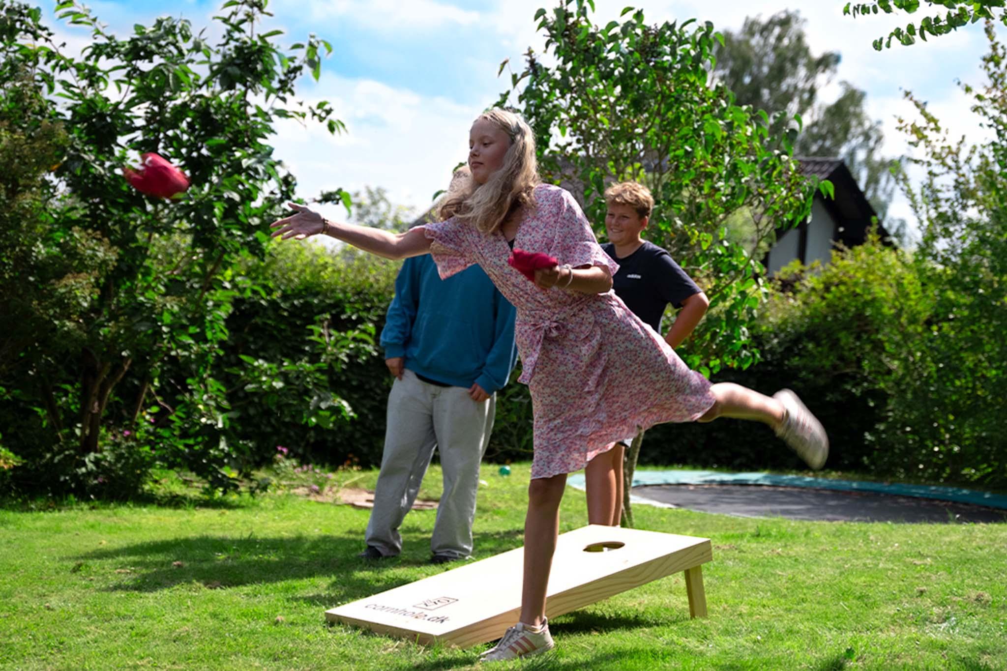 BÞrn som stÄr og spiller cornhole me det Cornhole SÊt - 120x60 cm (Officielle mÄl) fra Cornhole.dk.
De spiller ude i haven hvor man kan se det grĂžnne grĂŠs og solen skinner.